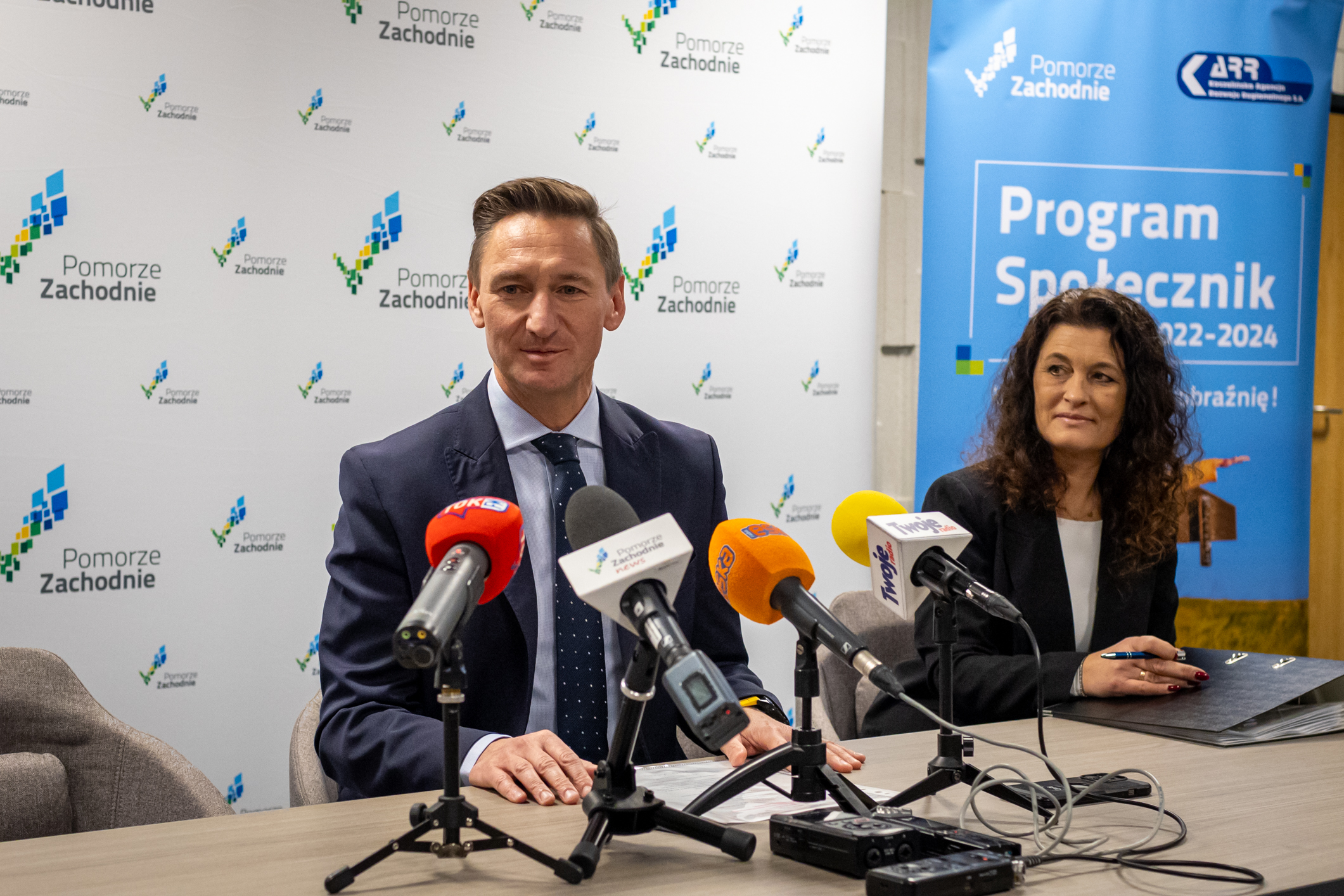 Społeczniczki i Społecznicy z pierwszymi umowami na 2024 rok. Marszałek Geblewicz i prezes KARR Natalia Wegner dziękują społecznikom za złożone wnioski, w tle ścianka promocyjna Pomorza Zachodniego.